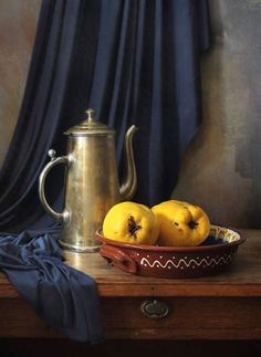 two lemons in a bowl next to a silver tea pot