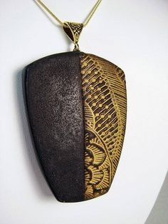 a wooden pendant with an intricate design hanging from a gold chain on a white wall