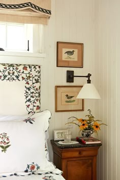 a bed sitting under a window next to a lamp and a table with flowers on it