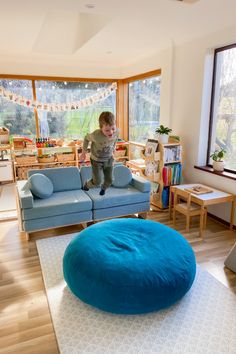 a young boy jumping on top of a blue bean bag chair in a living room