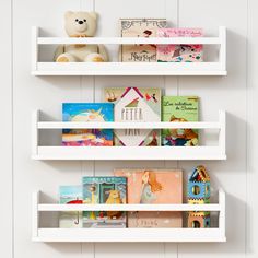 three white shelves with books on them and a teddy bear in the middle one shelf is filled with children's books