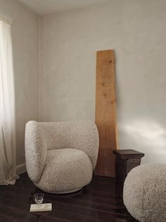 a chair and ottoman in a room with wood flooring, white walls and curtains