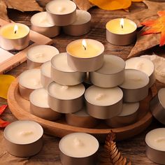 many lit candles on a wooden tray surrounded by autumn leaves