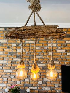 three light bulbs hanging from a wooden beam on a brick wall with ropes and rope