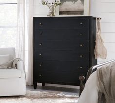 a bedroom with a white chair and black dresser