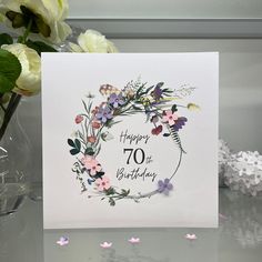 a birthday card with flowers and butterflies in the center, on a table next to some confetti