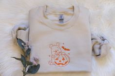 a t - shirt with a teddy bear and pumpkin on it sitting next to some flowers