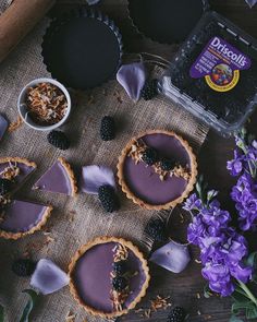 some pies are sitting on a table with purple flowers and blackberries next to them