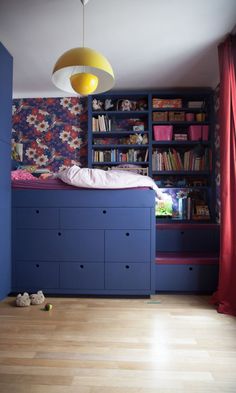 a bedroom with blue bookcases and wooden flooring next to a red curtain