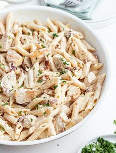 a pasta dish with chicken and parsley in a white bowl on top of a table