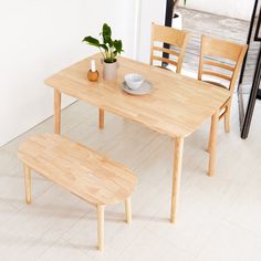 a wooden table with two chairs and a plant on it in front of a white wall