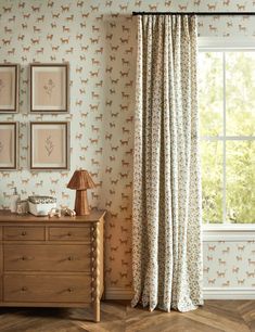 a room with a dresser, window and wallpaper on the walls that has deers printed on it