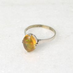 "A rainbow is swimming in this gorgeous antique opal ring! A beautifully proportioned opal cabochon is centered with cardinal prongs (north, south, west and east) in an 18k white gold setting. The opal features a transparent orange body, typical of Mexican jelly opals, with a \"contra luz\" color flash seen when the gem interacts with light. The color play is astounding, with every color of the rainbow ignited within the body of the opal, having painterly brush-stroke like patterns. This ring hails from the 1920s and has been tenderly well-cared for in its lifetime. It is in wonderful condition and ready for a new owner. This ring could be a perfect alternative engagement ring, gift for someone with an October birthstone or simply a present for an antique jewelry lover.   Opal is a fascina Vintage Opal Ring As A Gift, Antique Style Opal Ring For Formal Occasions, Vintage Opal Round Rings, Antique Style Round Opal Ring, Heirloom Style Collectible Opal Ring, Vintage Opal Rings In Yellow Gold, Oval Ethiopian Opal Ring For Anniversary, Heirloom Opal Ring Collectible, Heirloom Opal Ring