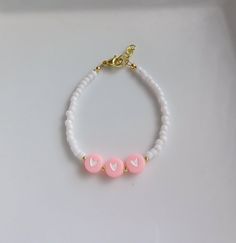 two pink and white beads on a gold plated charm bracelet with heart shaped beads