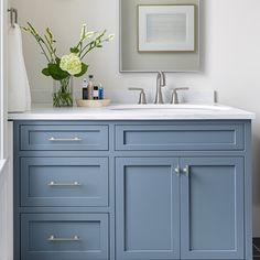 a bathroom with blue cabinets and white counter tops, framed pictures on the wall above it