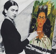 a woman is holding a brush in front of a painting