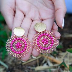 a pair of pink and gold earrings in someone's hand with their fingers on the ground