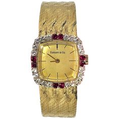 This elegant champagne dial 14K Yellow Gold Tiffany & Co. wristwatch with a cushion shaped diamond bezel, is set with 2 brilliant rubies at the 12 o'clock, 3 o'clock, 6 o'clock, and 9 o'clock positions .The head measures 7/8 inch wide (not including the crown). The integral, patterned gold band has two settings: one at 6 5/8 inches long and one at 6 7/8 inches long. The 24 round brilliant cut diamonds weigh an approximate total of 1.00CT of overall G Color and VS1 Clarity. The 8 rubies weigh an Gold Tiffany, Bezel Watch, Gold Diamond Watches, Art Deco Watch, Gold Watches, Gold Watches Women, Color Champagne, Tiffany And Co, Bezel Diamond