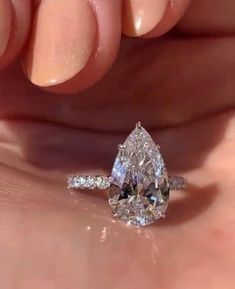 a woman's hand holding an engagement ring with a pear shaped diamond