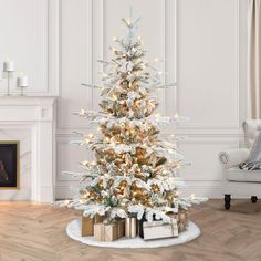 a white christmas tree with gold and silver presents under it in a living room setting