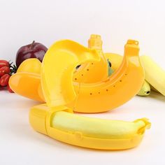 a banana peeler sitting next to bananas and other fruit on a white table top