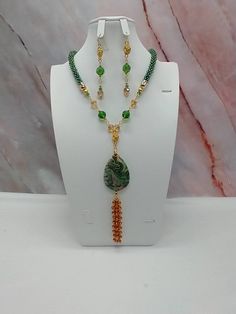 "Handmade and designed by me-one of a kind necklace set-green rainbow seed bead crocheted rope necklace-19\"-5\" long focal with a Mexican crazy lace agate pendant bead and a 3\" seed bead beaded tassel-green and tan glass beads-rose connectors-2 3/4\" long matching dangle earrings-gold tone findings-lobster clasp-1\" extender chain. Add this beautiful necklace set to your jewelry collection-would be an eye catching set for a summer night!" Handmade Gold Jade Beaded Necklaces, Elegant Green Beaded Long Crystal Necklace, Green Beaded Long Crystal Necklace, Long Green Beaded Crystal Necklace, Handmade Green Crystal Long Necklace, Bohemian Green Crystal Necklace With Colorful Beads, Green Multi-strand Jewelry For Gift, Unique Handmade Double Strand Beaded Necklaces, Handmade Unique Double Strand Beaded Necklaces