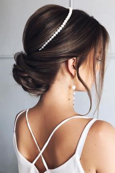 a woman with her hair in a low bun, wearing a white top and pearl earrings