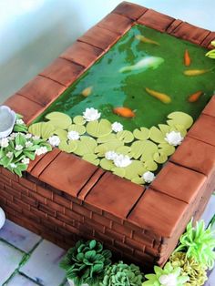 a cake that is shaped like a pond with goldfish in it and flowers on the side