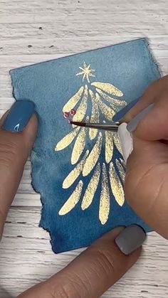 someone using scissors to paint a christmas tree on a piece of blue paper with gold foil