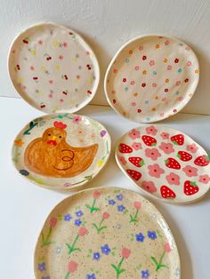 four plates with designs on them sitting next to each other in the shape of chickens and flowers