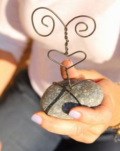 a woman holding a rock with a wire sculpture on it's top and two hands