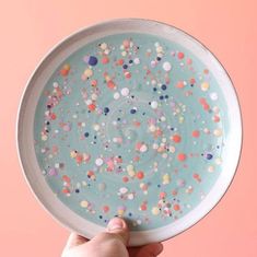 a hand holding a plate with sprinkles on it in front of a pink background