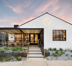 a white building with black windows and stairs leading up to the front door that leads into an outdoor dining area