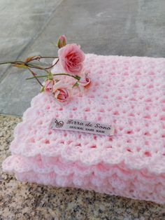 a pink crocheted blanket sitting on top of a stone floor next to a flower