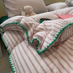 a bed with pink and white striped sheets, pillows and a teddy bear on it