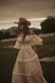 a woman in a white dress and cowboy hat poses for the camera with her hands on her hips