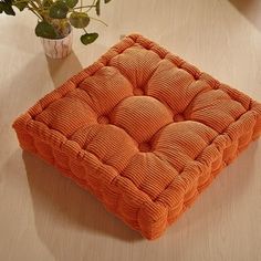 an orange cushion sitting on top of a wooden table next to a potted plant