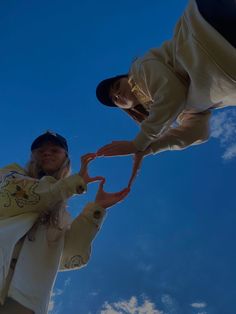 two people standing next to each other in front of a blue sky with white clouds