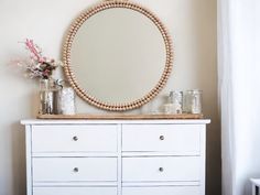 a white dresser topped with a round mirror