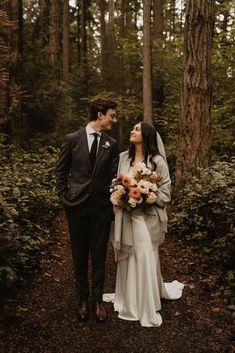 a bride and groom standing in the woods