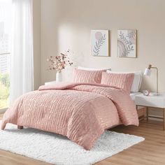 a bed with pink comforter and pillows on top of it in a room next to a window