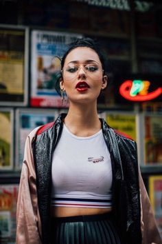 a woman wearing glasses and a crop top standing in front of a wall with posters on it