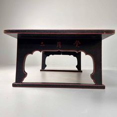 a small wooden table with chinese writing on the top and bottom section, sitting on a white surface