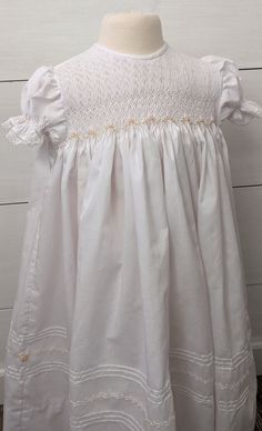 Beautiful smocked christening dress and bonnet. Size 6-12 months is ready to ship! This beautiful set has a smocked bodice with beautiful flower details.  Smocked sleeves, pin tucking on the dress with hand feather stitching and flower clusters are just a few special details.  Two buttons close the back. The beautiful smocked bonnet has a row of 29 bullion roses!  Fabric ties tie under baby's chin. Pretty pintucks and a single rose are on each tie end.   Dress measures 23 1/2 inches from shoulde White Smocked Dress, A Single Rose, Blessing Dress, Feather Stitch, Christening Dress, Single Rose, Smocked Dress, Beautiful Flower