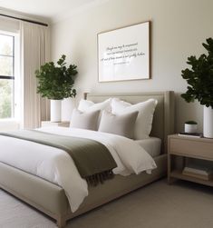 a bed with white sheets and pillows in a bedroom next to a large window filled with potted plants