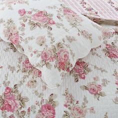 a bed with pink flowers on it and a quilted coverlet in the background