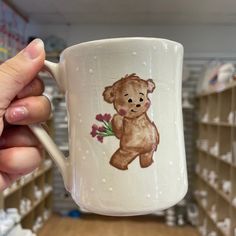 a person holding up a coffee mug with a teddy bear on it in a store