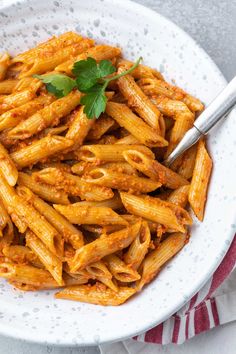 a white bowl filled with pasta and sauce on top of a red and white towel