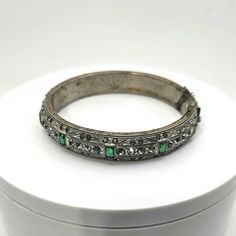 Vintage to antique art deco era hinted bangle bracelet. This features white paste rhinestones all around with emerald green accent stones. There is beautiful detail on the etched metal edges. interior shows wear as pictures. The newer safety clasp needs to be replaced. Still a stunning and rare find. Expedited shipping is available by request on a case by case basis. Please message us if you require rush shipping. Returns are are accepted within the time window noted. To recieve a full refund th Vintage Green Bangle For Wedding, Vintage Jeweled Bangle, Vintage Jeweled Bangle Bracelet, Vintage Jeweled Bangle For Wedding, Vintage Jeweled Wedding Bangle, Silver Jeweled Bangle For Formal Occasions, Vintage Jeweled Bangle Cuff Bracelet, Vintage Jeweled Cuff Bracelet, Vintage Green Cuff Bracelet For Formal Events