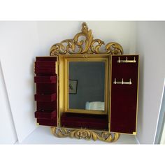 an ornate gold framed mirror on the wall above a red velvet drawer and shelf with drawers